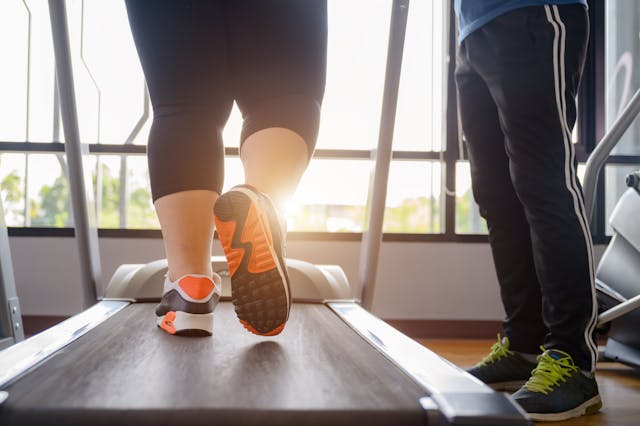 Woman walking on treadmill with trainer standing by | Image credit: ID_Anuphon – stock.adobe.com