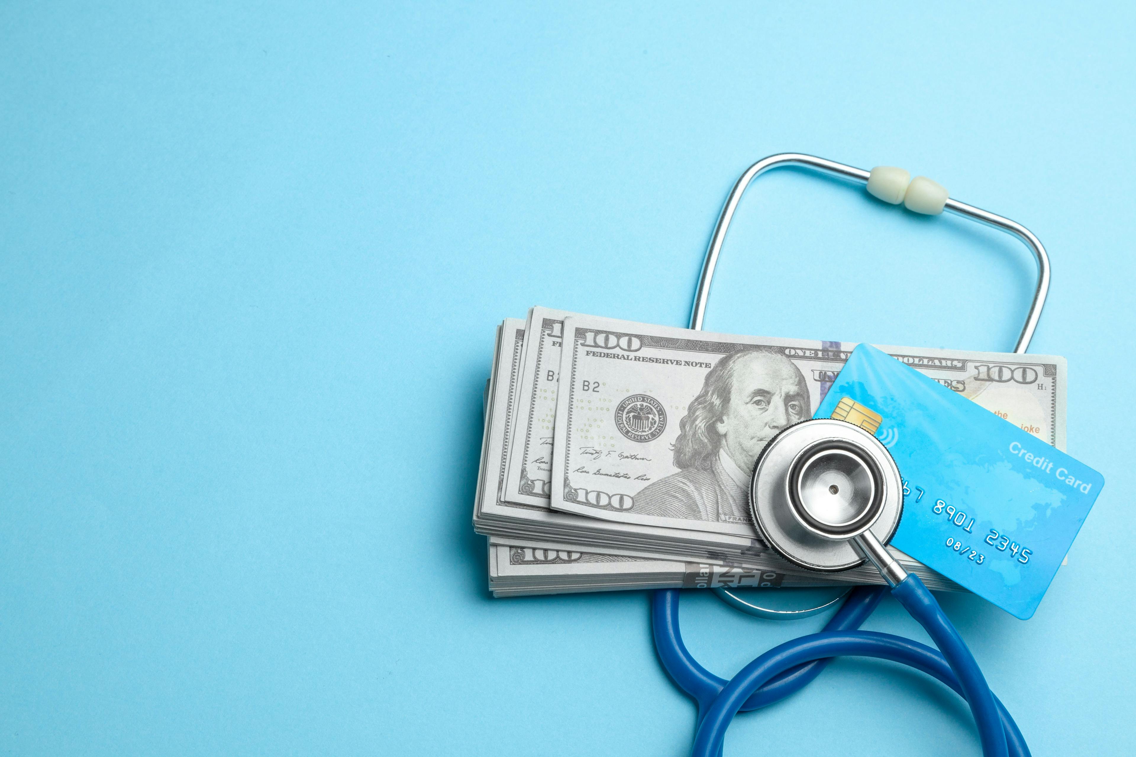 Cash and credit card with a stethoscope on a blue background | Image credit: adragan - stock.adobe.com