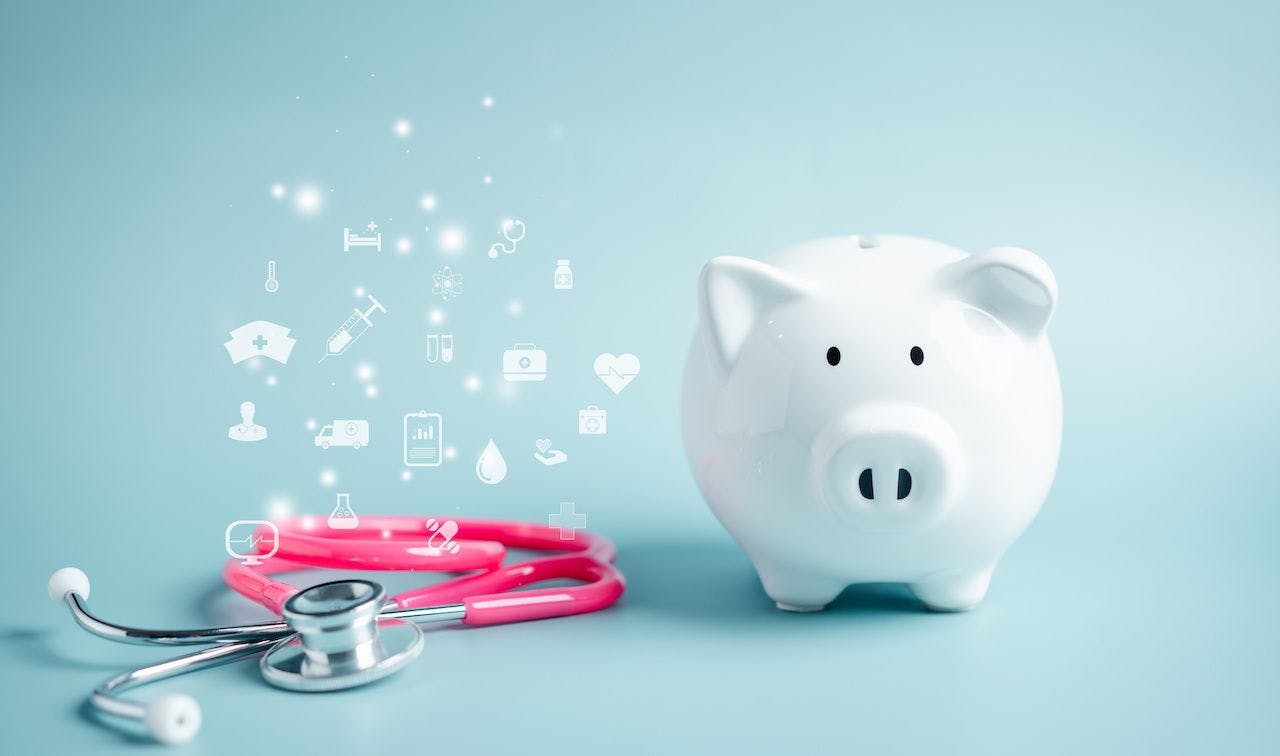 White piggy bank next to a pink stethoscope and various health care icons | Image credit: Kiattisak - stock.adobe.com