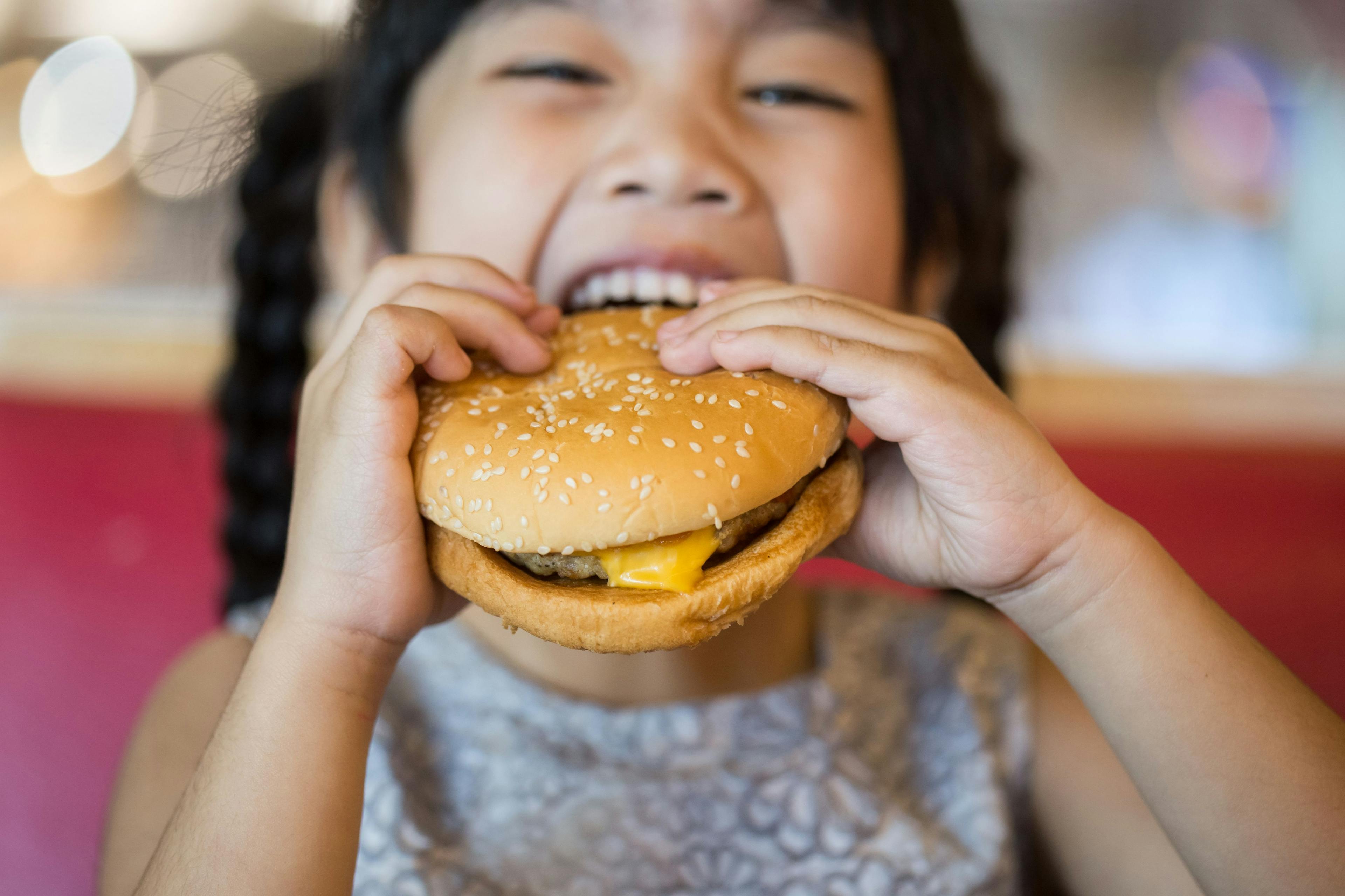 Child eating fast food cheeseburger | Image credit: escapejaja – stock.adobe.com
