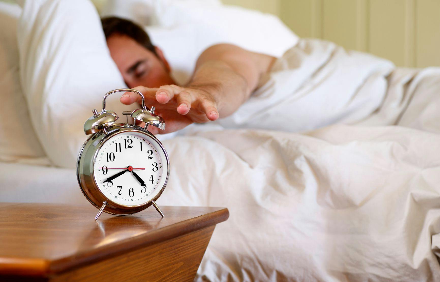 person in bed hitting alarm clock