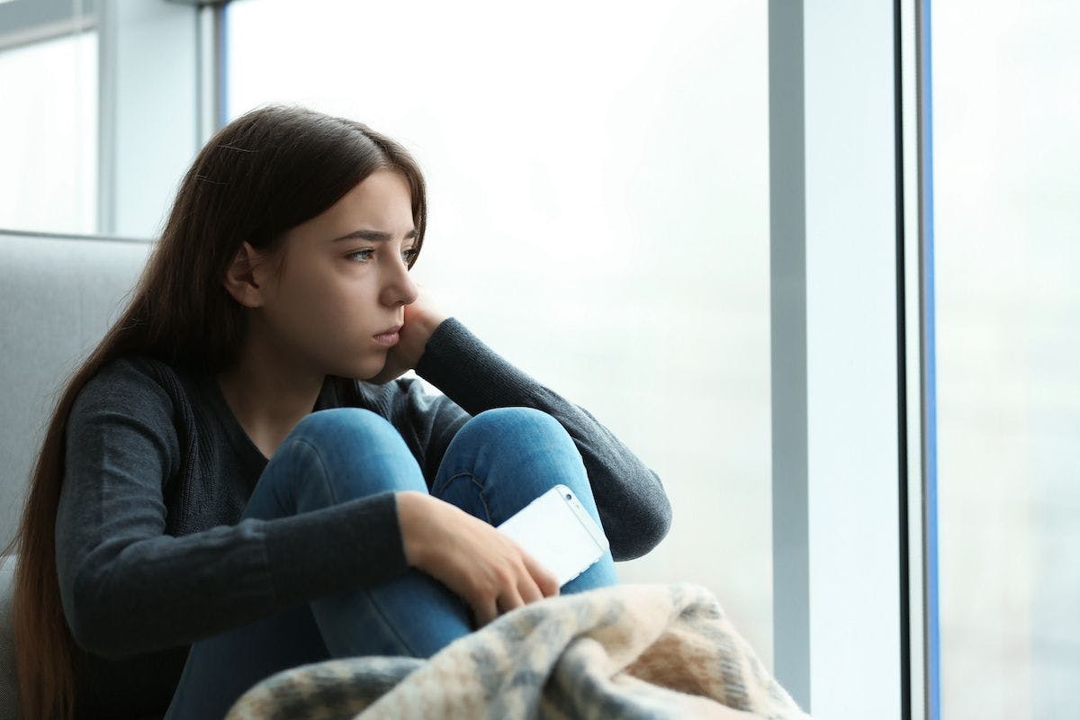 Depressed teen girl with smartphone | Image Credit: © New Africa - stock.adobe.com