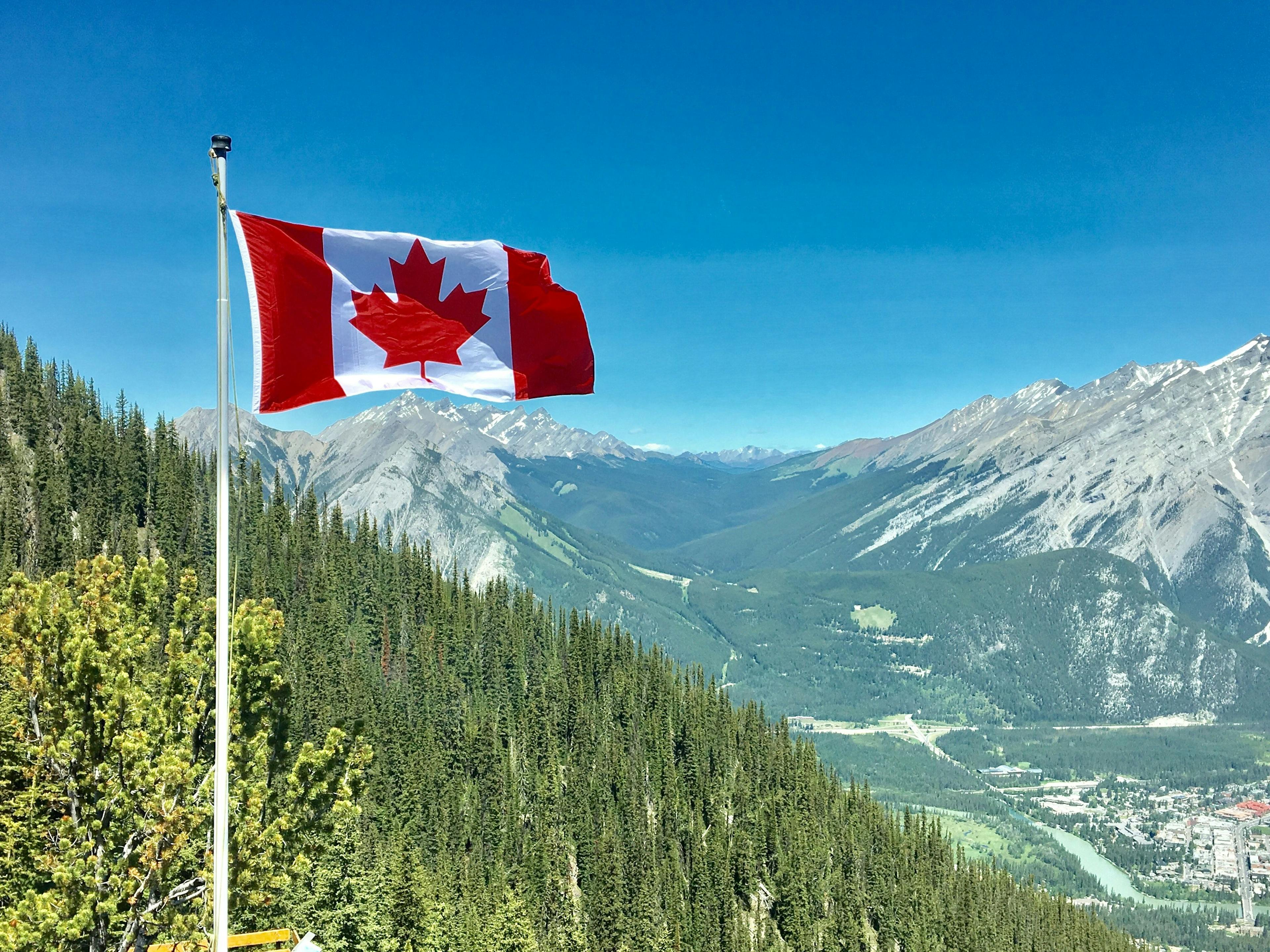 Canadian flag on a flag pole with mountain landscape in the background