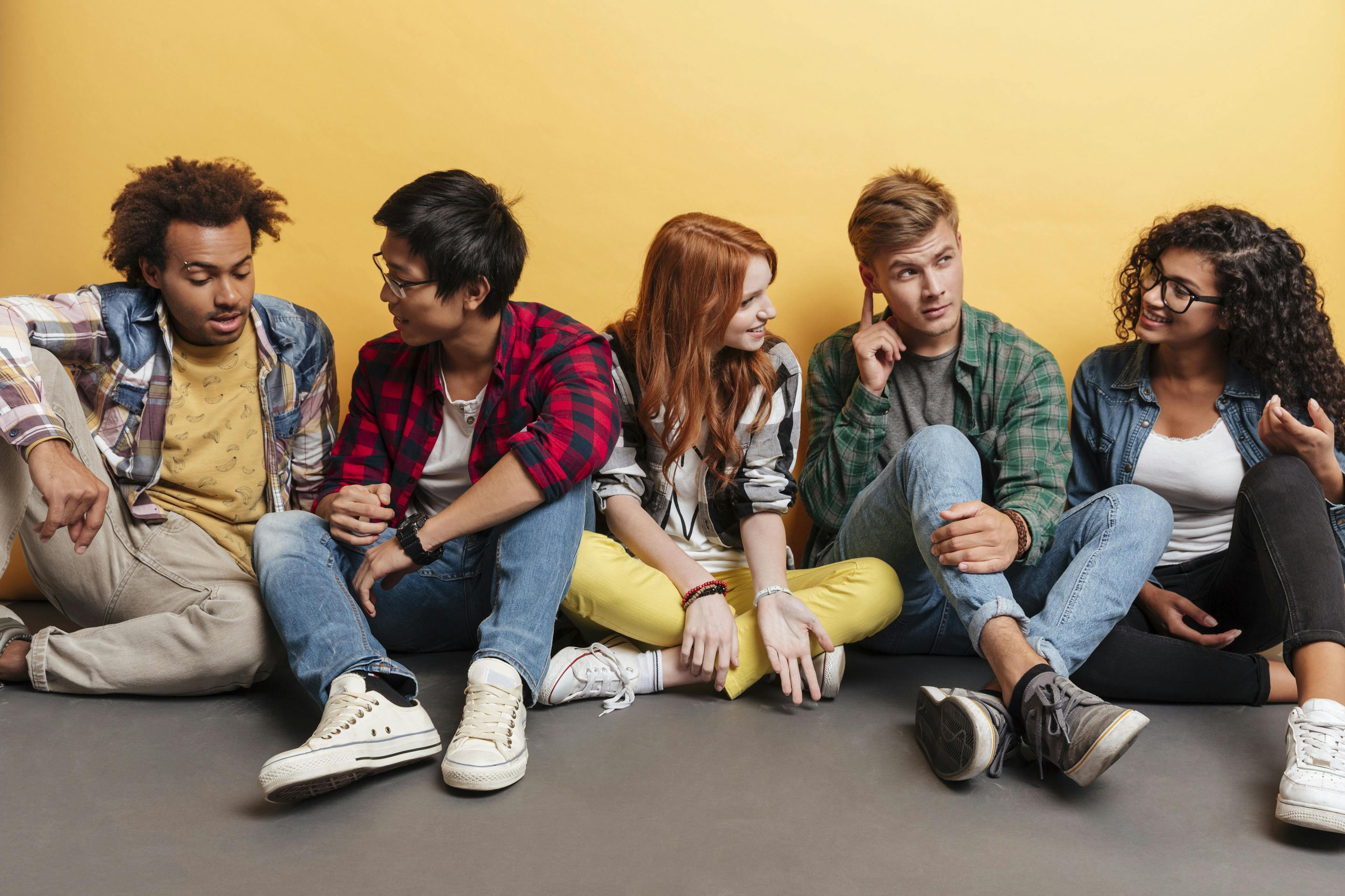 group of 5 teens sitting on floor talking
