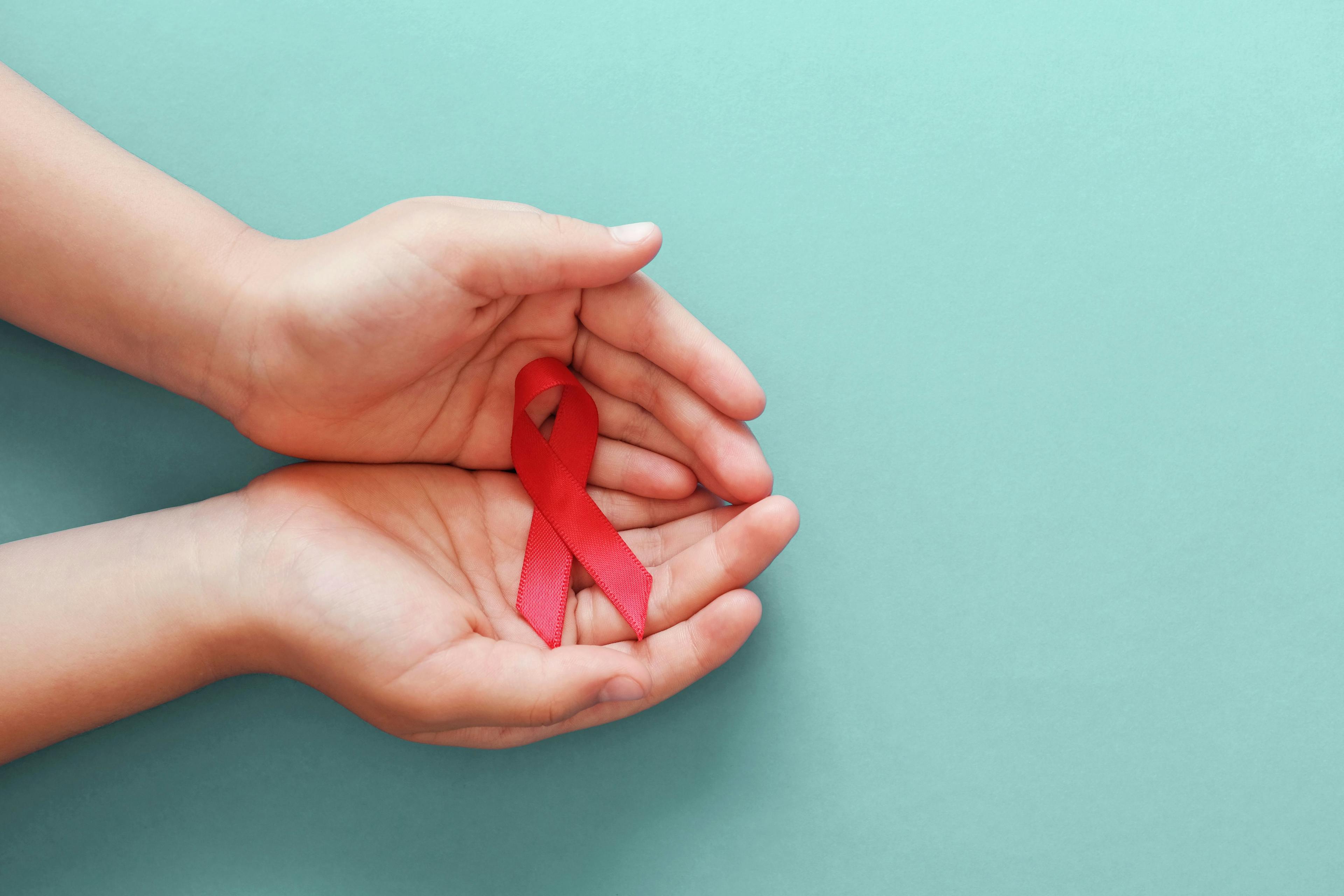 Hands holding red ribbon for HIV Awareness | Image credit: SewcreamStudio - stock.adobe.com