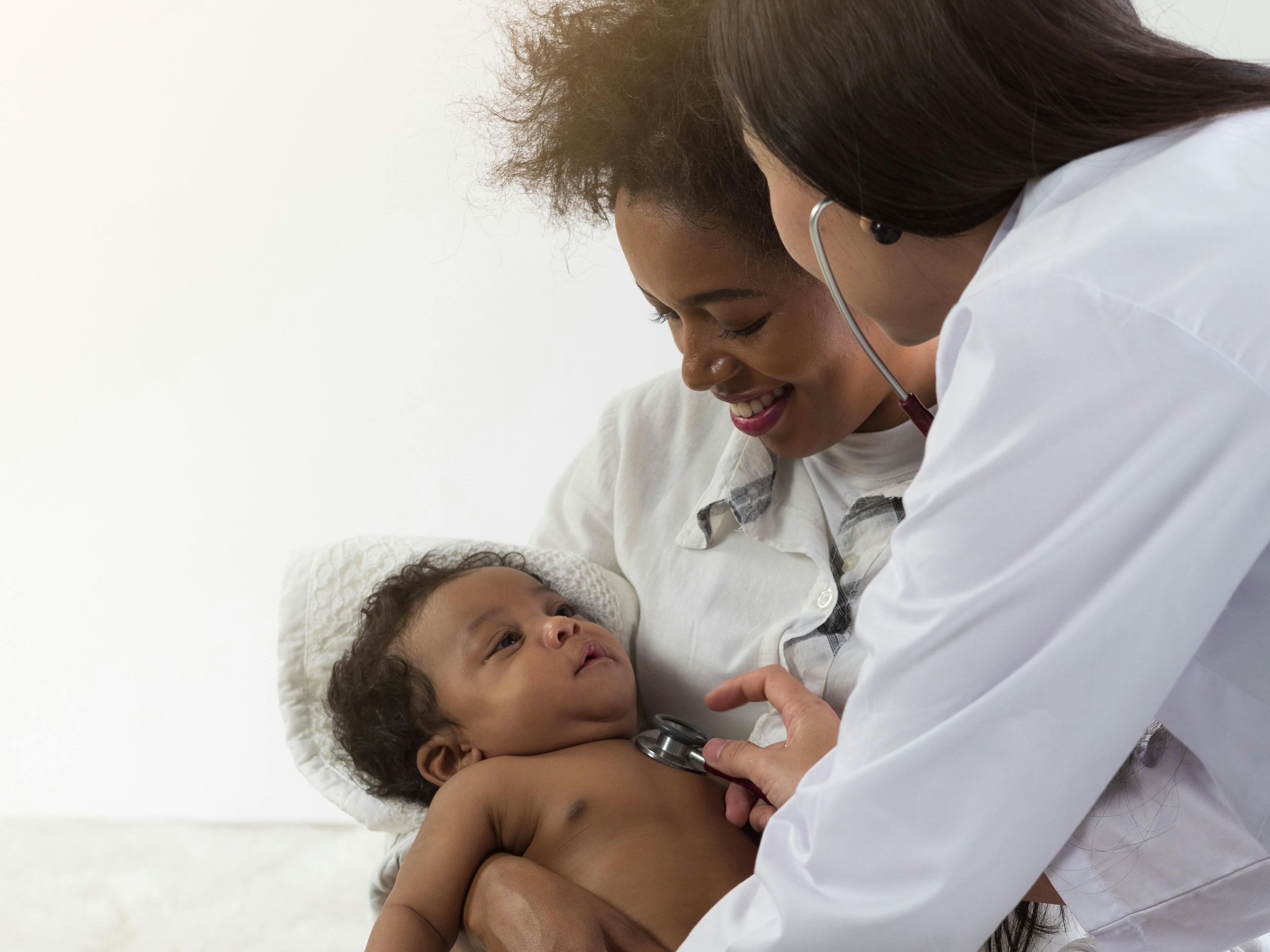 Asian doctor checking on African baby boy in mother's arms | Image credit: Dollydoll - stock.adobe.com