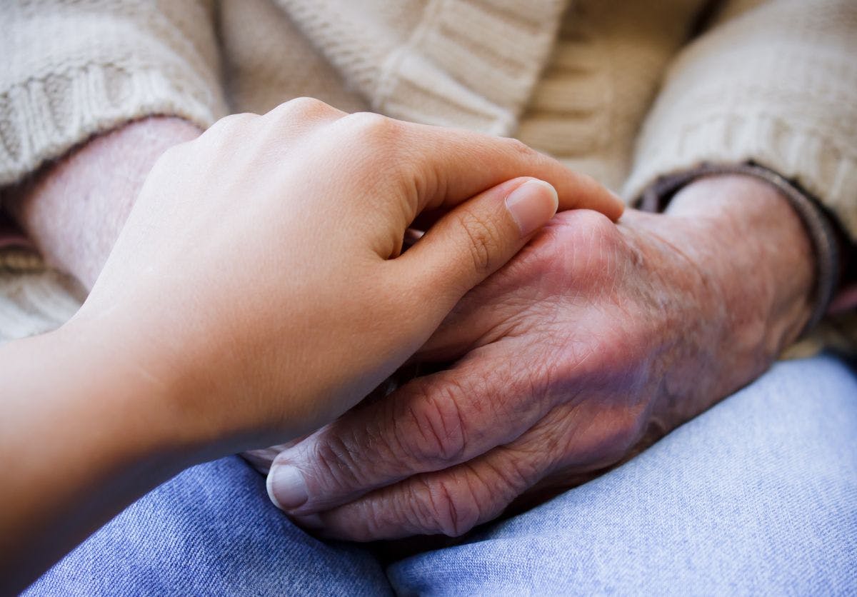 An older person's hands are on their lap while a younger person's hands cover them