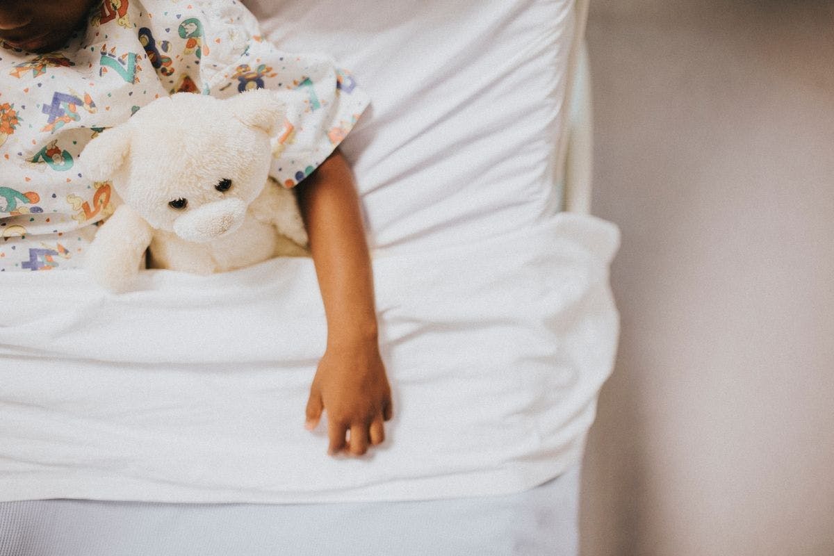 Partial photo of child in bed with teddy bear