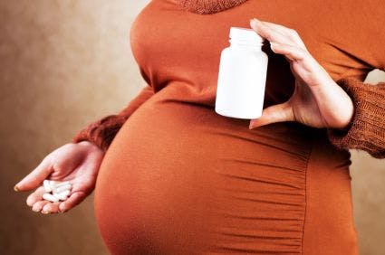 pregnant woman holding a pill bottle in one hand and pills in the other