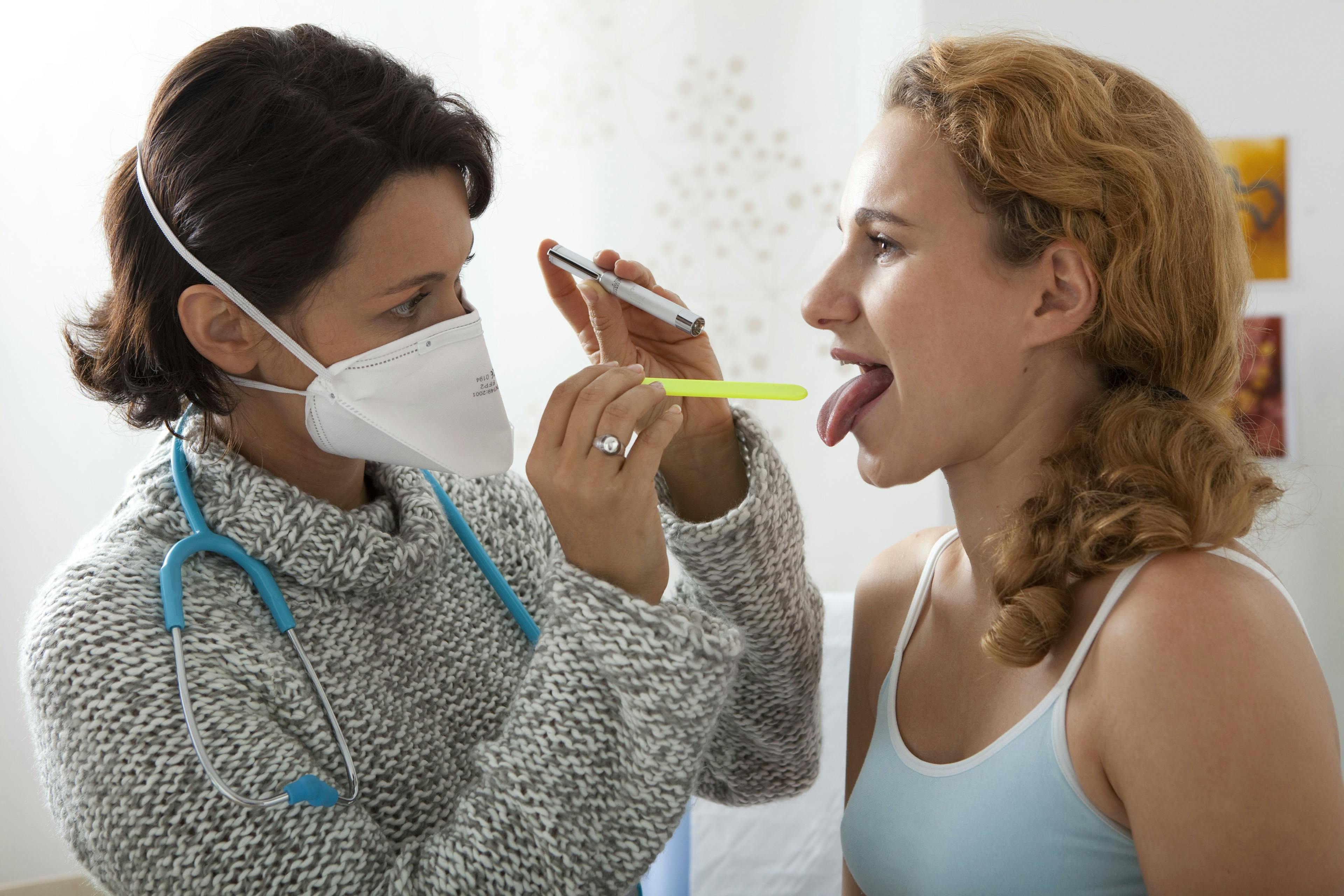 woman having her throat examined by a doctor who is wearing a face mask