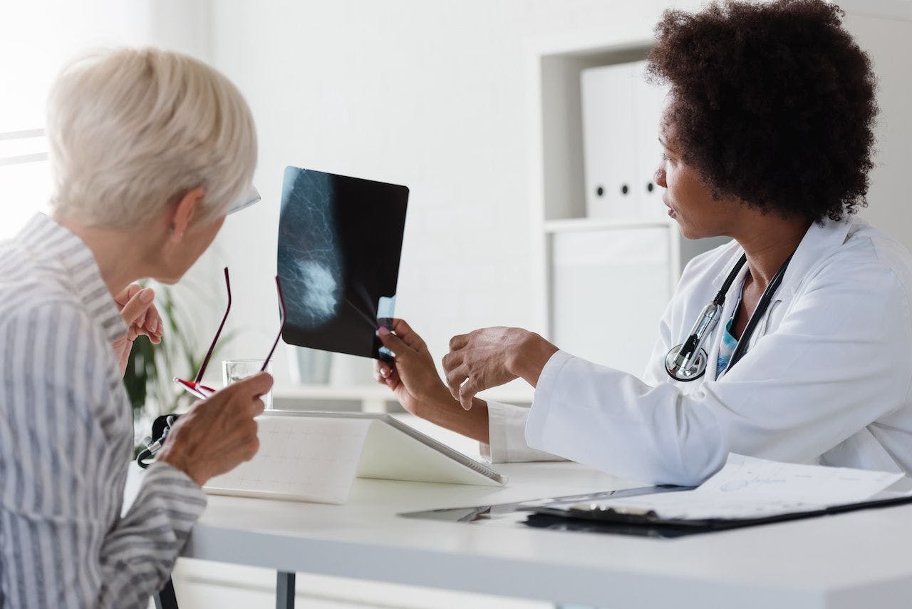 A female doctor sits at her desk and talks to a female patient while looking at her mammogram. Braest cancer prevention | Image Credit: lordn - stock.adobe.com