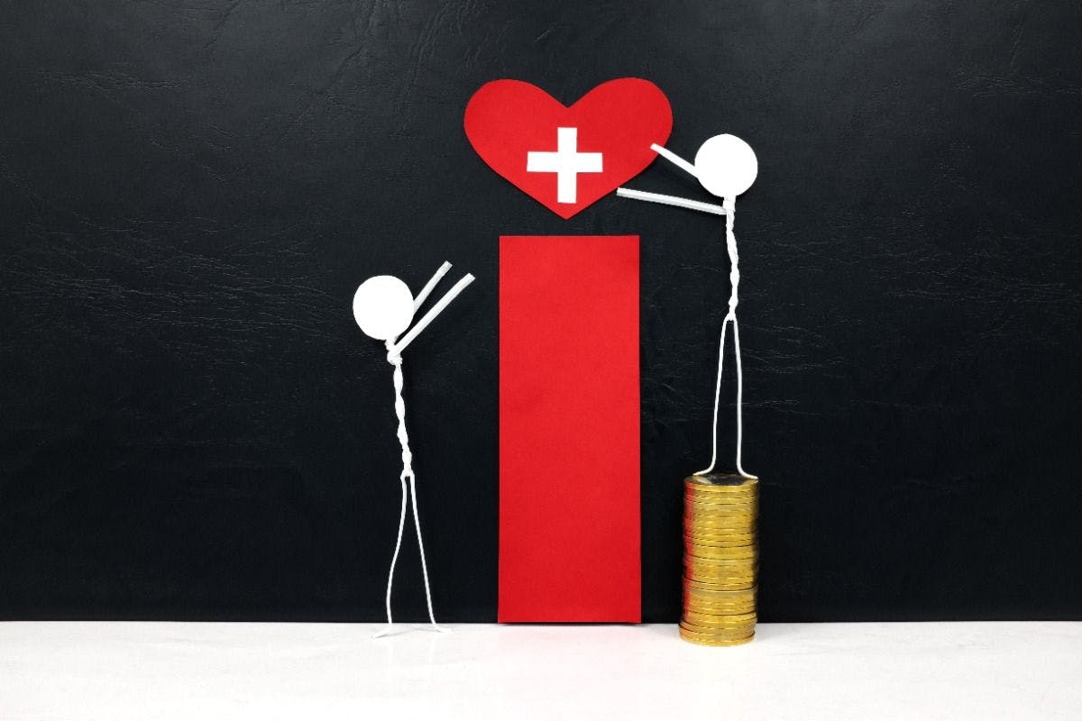 Stick man figure reaching for a red heart shape with cross cutout while stepping on stack of coins. Health, healthcare, medical care and hospital access inequality concept. | Image Credit: © sulit.photos - stock.adobe.com