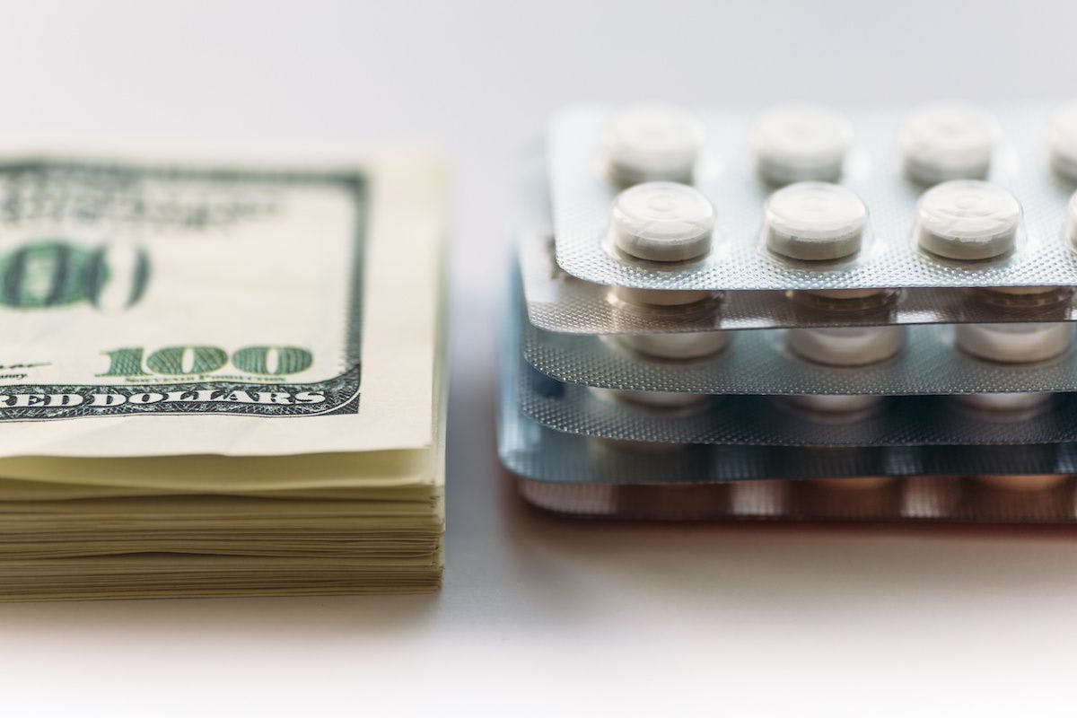 stack of $100 bills next to stack of pills