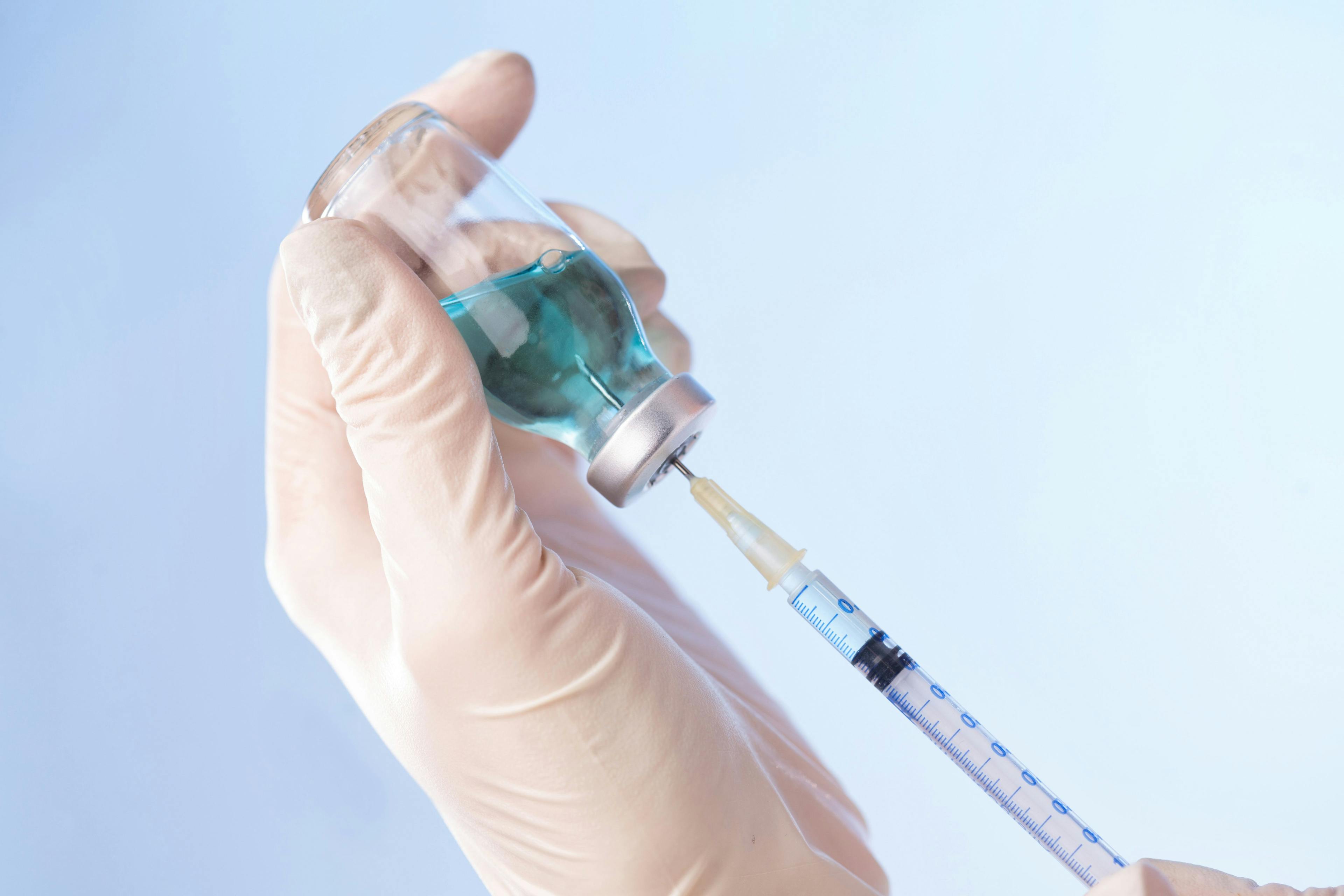 person wearing rubber gloves filling a subcutaneous syringe with a teal liquid