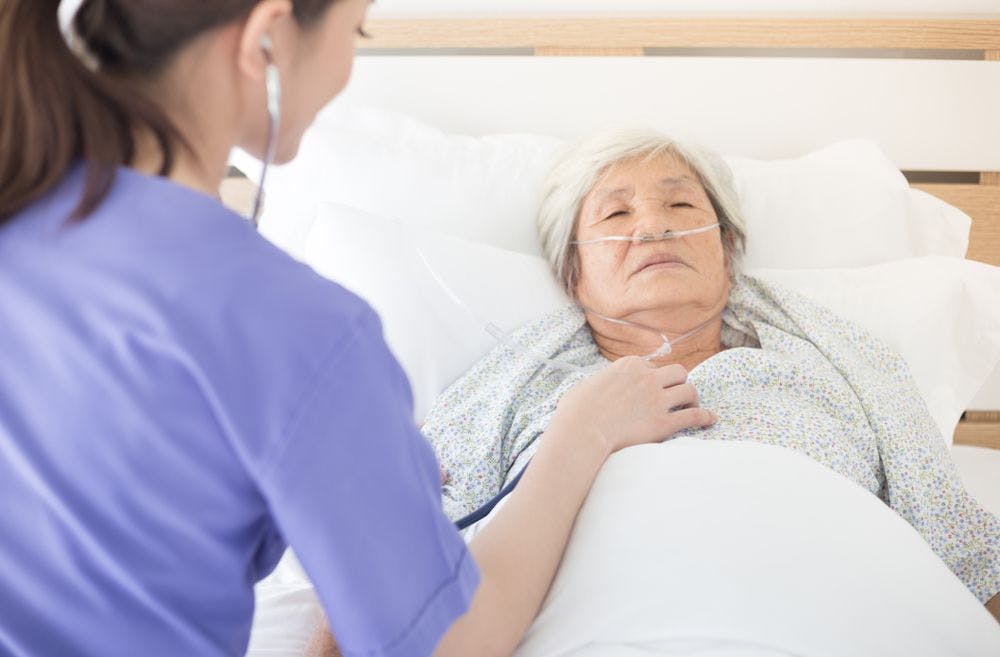 woman in hospital bed receiving oxygen and having her heartbeat checked by a doctor