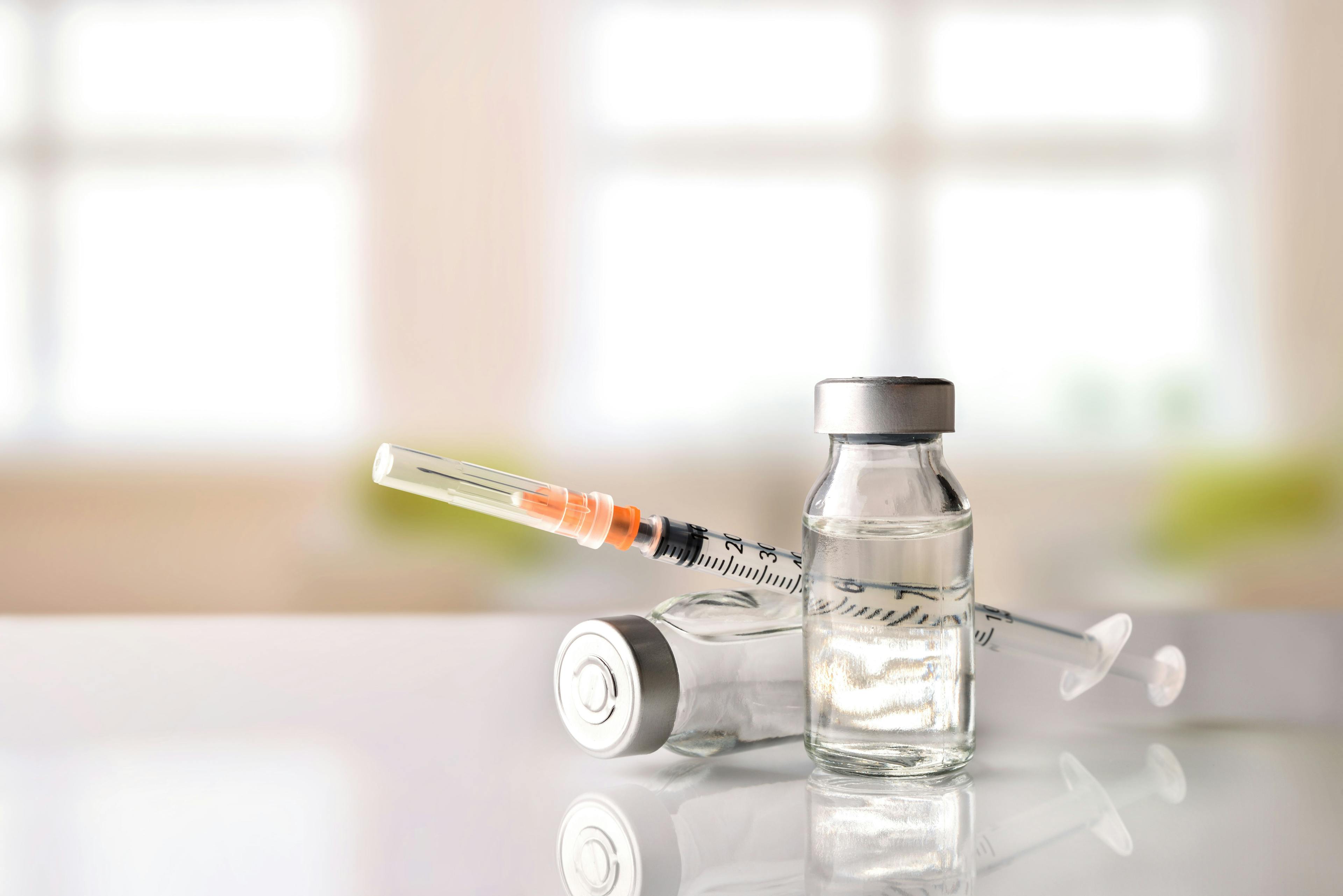 Vials and syringe on white table with background windows | Image Credit – Davizro Photography - stock.adobe.com