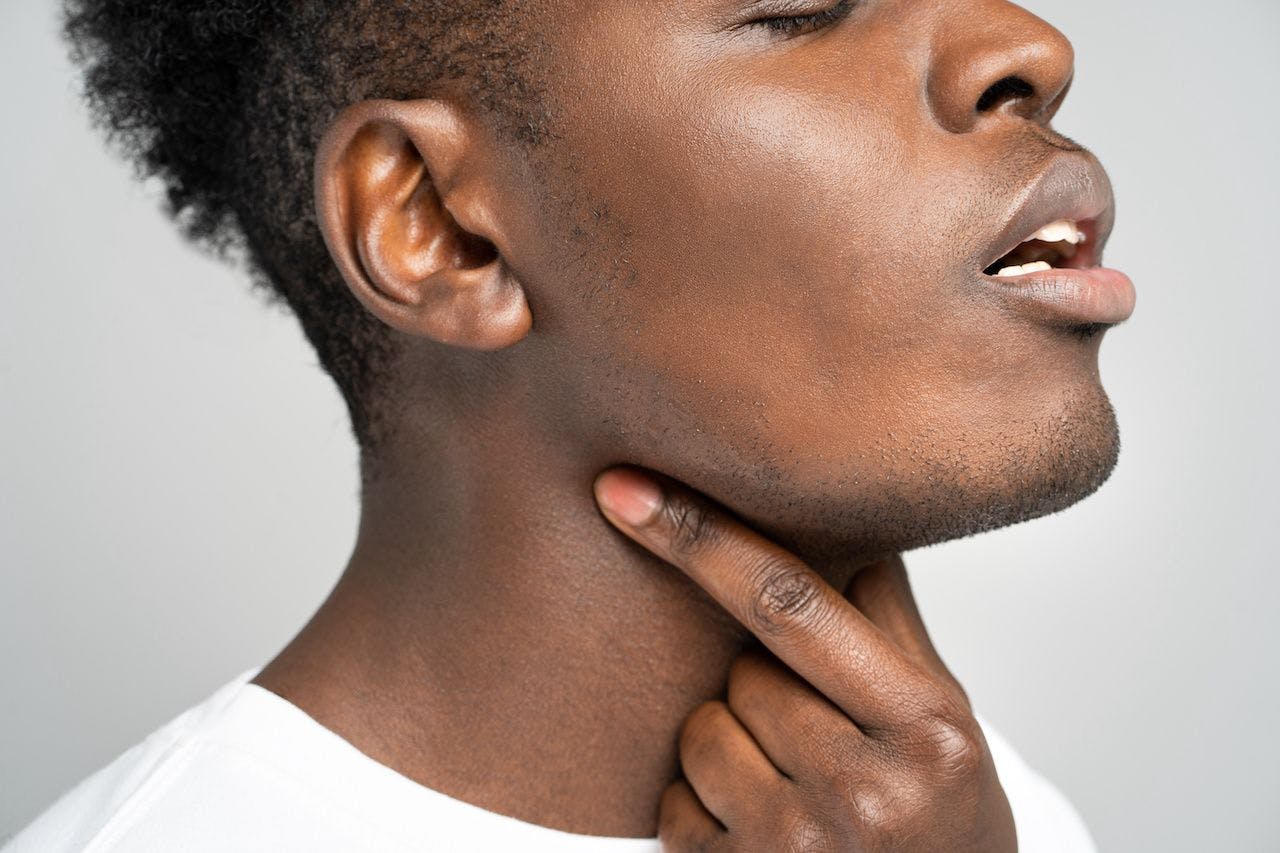 Closeup of afro man touches fingers of sore throat, isolated on gray background. Thyroid gland, painful swallowing, tonsillitis, laryngeal swelling concept. Inflammation of the upper respiratory tract: © DimaBerlin - stock.adobe.com