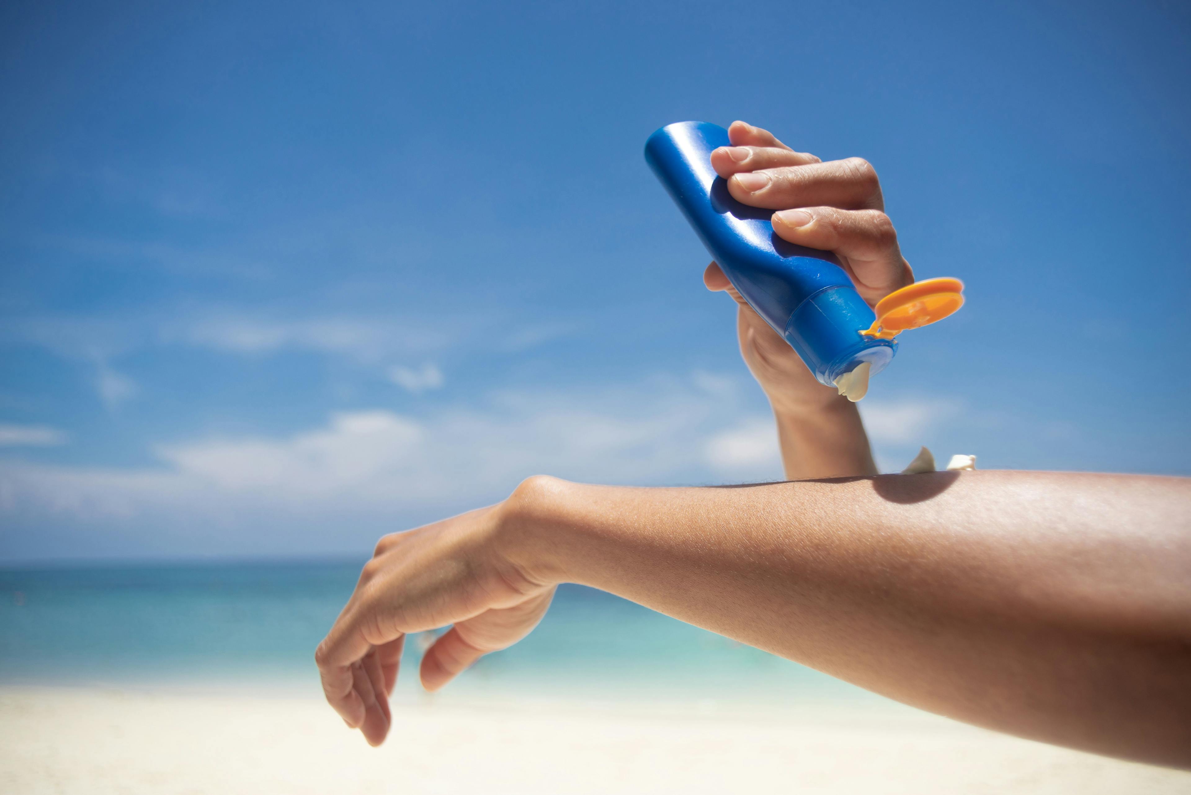 woman applying sunscreen to her arm on the beach | Image Credit: lesterman - stock.adobe.com