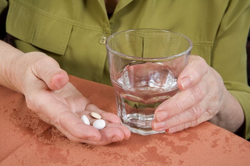 person holding white pills and glass of water