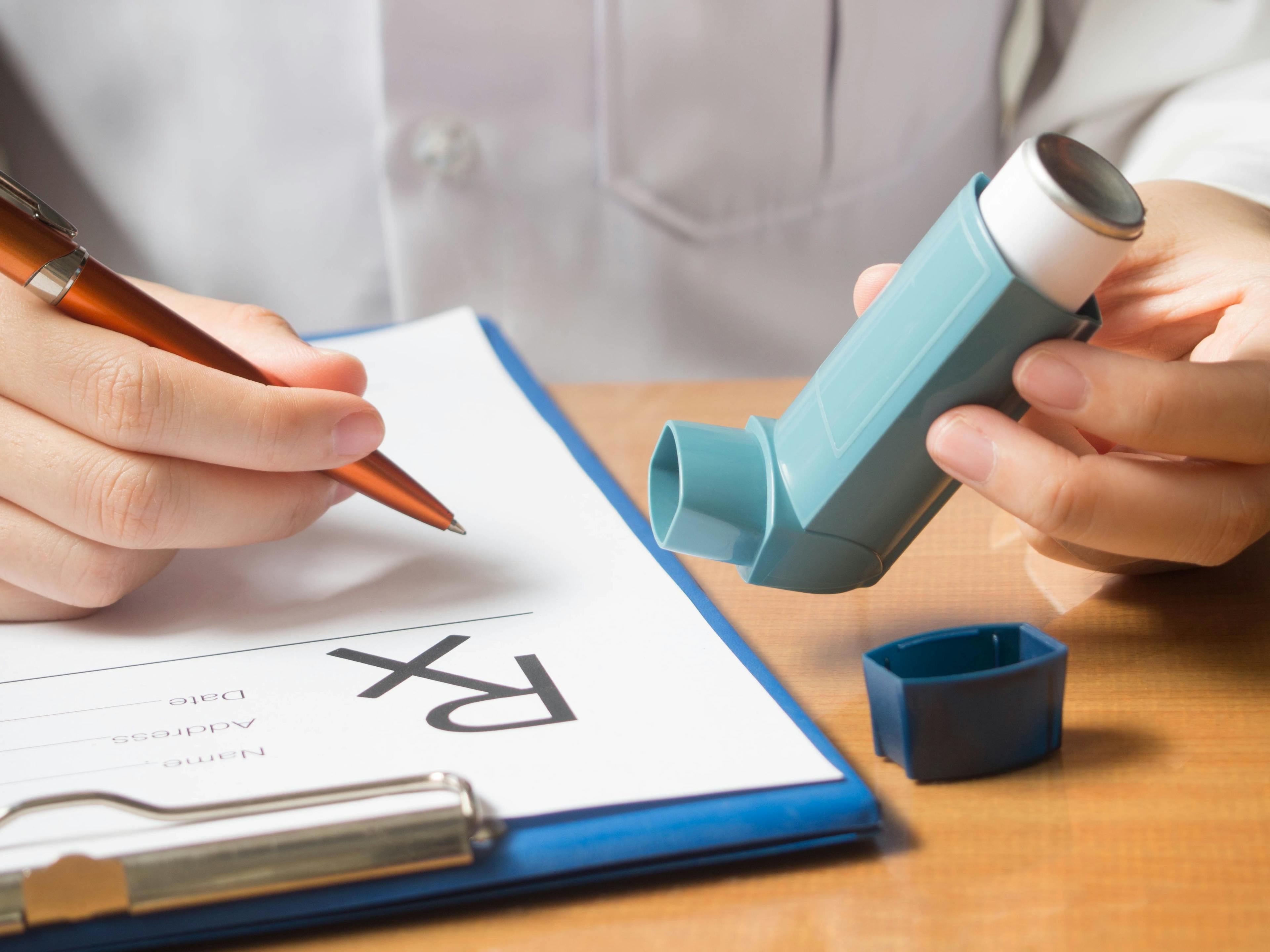 Close up of doctor hand holding blue asthma inhaler and writing medical prescription on rx form for treatment asthma | Image Credit: Orawan - stock.adobe.com