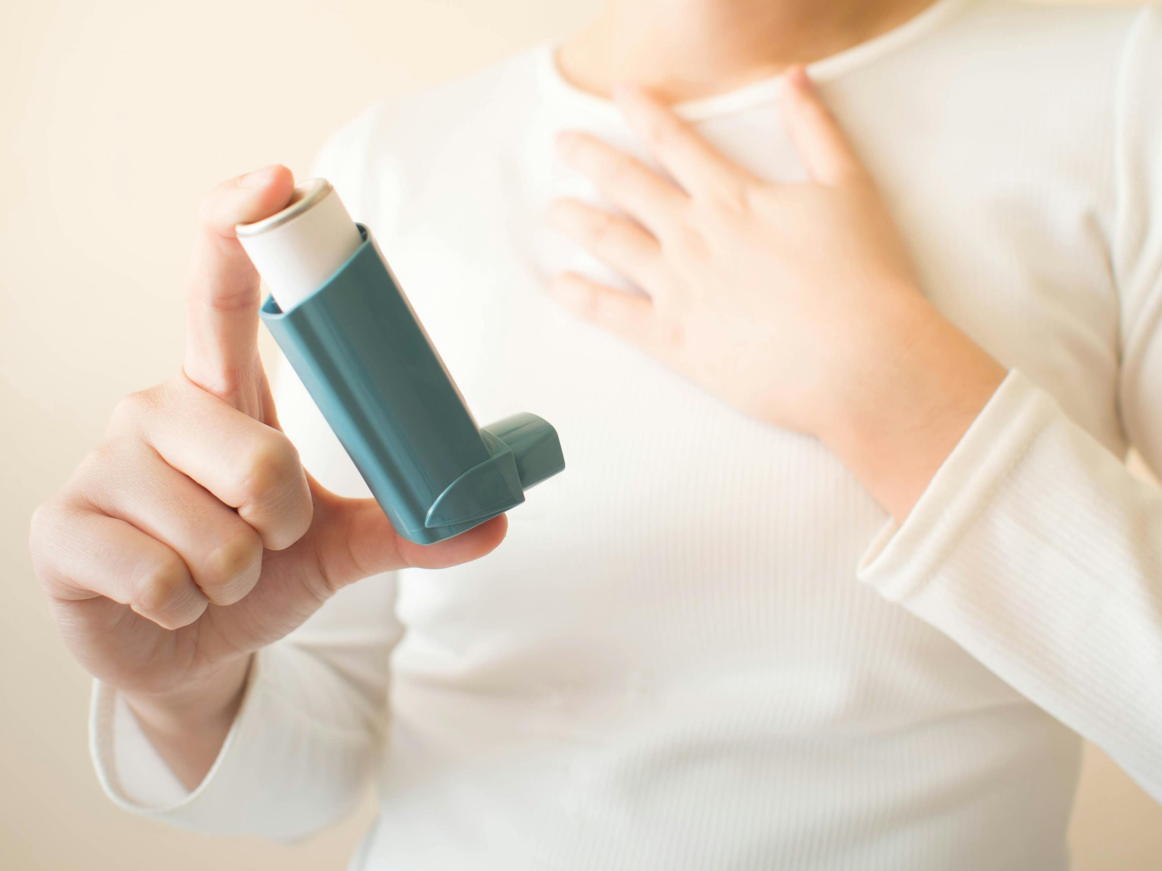 Young female in white t-shirt using blue asthma inhaler for relief asthma attack. Pharmaceutical products is used to prevent and treat wheezing and shortness of breath caused asthma or COPD. Close up | Orawan - stock.adobe.com