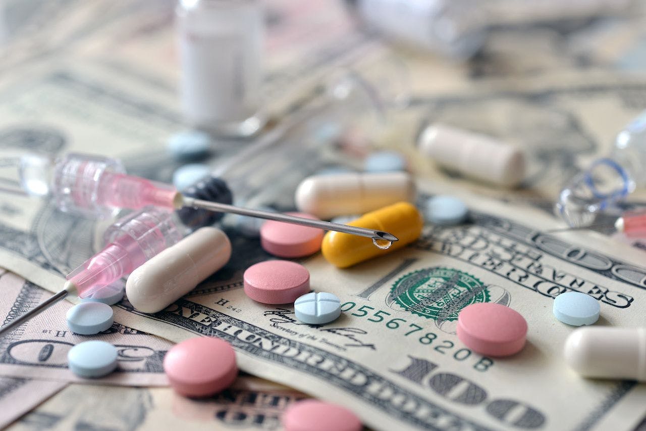Medicine on top of 100 dollar bills | image credit: Nikitos77 - stock.adobe.com